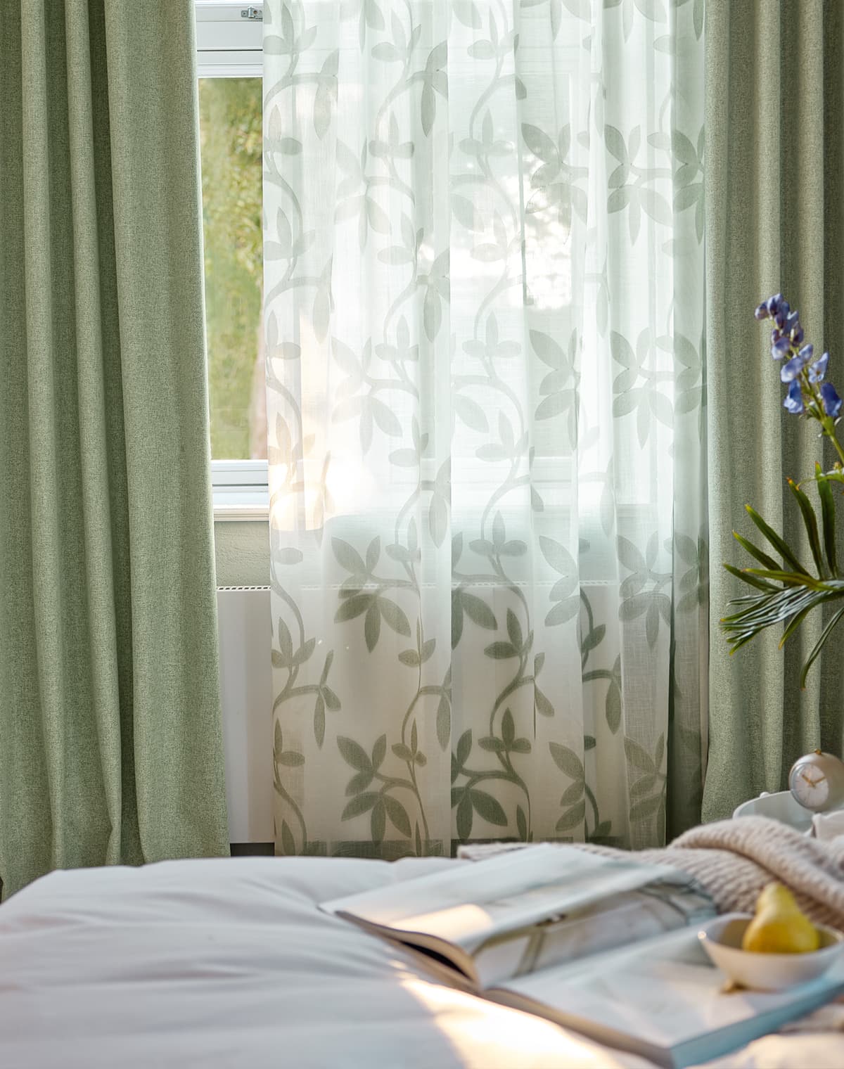 Eine grüne und eine transparente weiße Gardine mit floralem Muster im Schlafzimmer.