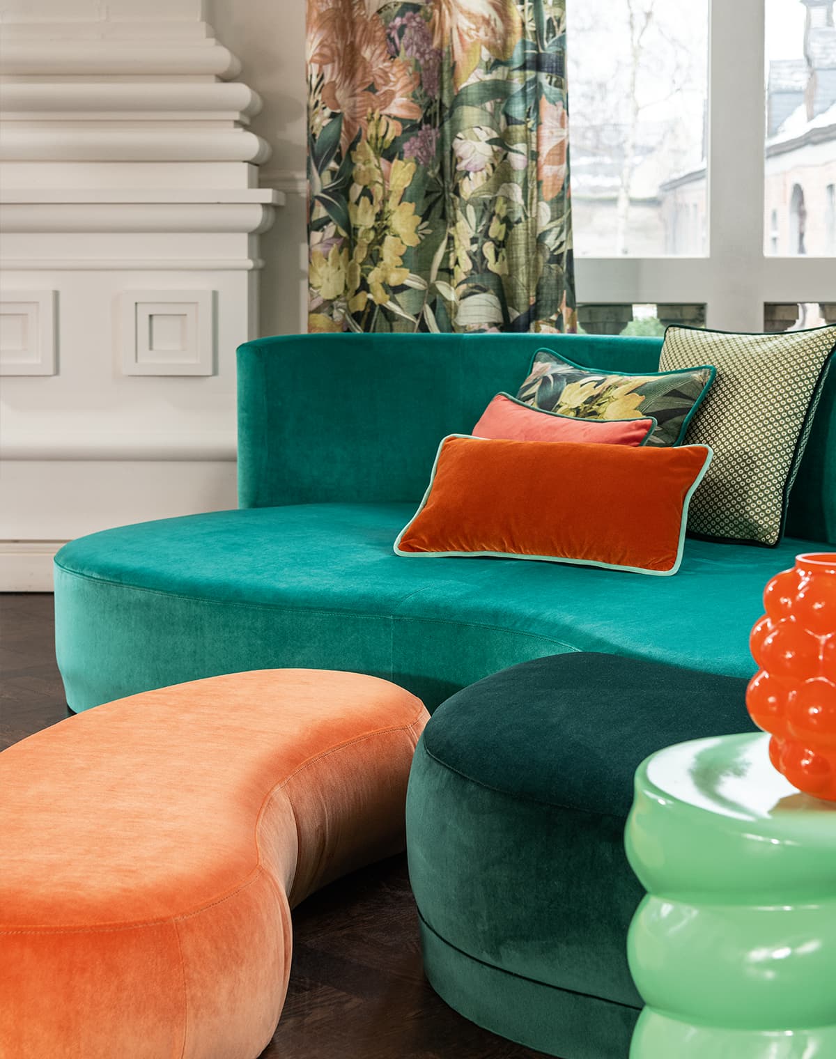 Ein grünes Sofa mit Kissen und ein Pouf in orange.