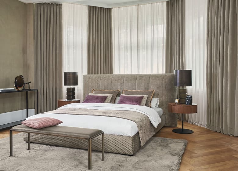 Ein Bett vor einer Reihe an braunen und weißen Vorhängen.