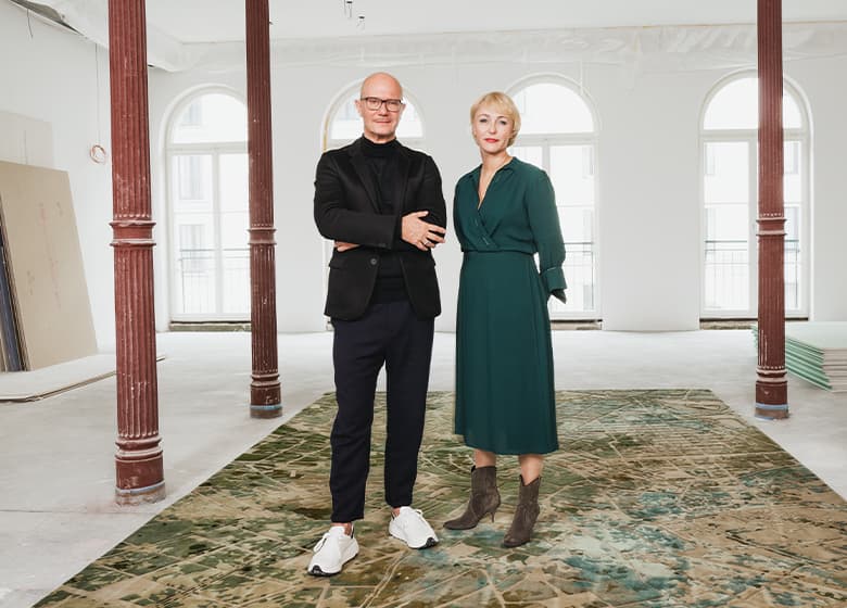 Zwei Designer, eine Frau und ein Mann stehen auf einem bunten Teppich in einem großen weißen Raum