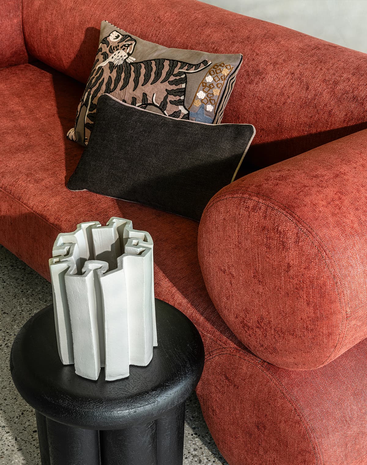 Schwarzer Beistelltisch, schwarzes Kissen, Kissen mit Tigerprint und ein rotes Sofa.