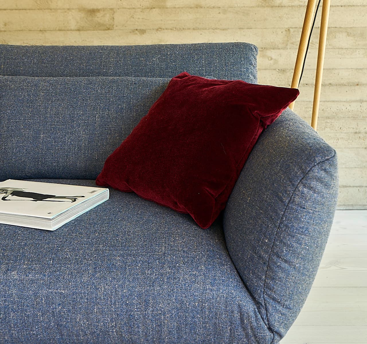 Detailaufnahme von dem Sofa Clou in blau melliert mit einem roten Kissen und einem weißen Buch darauf