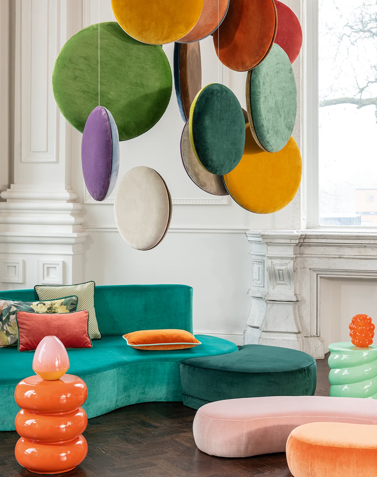 Ein grünes Sofa mit Kissen und Poufs in rosa und orange.