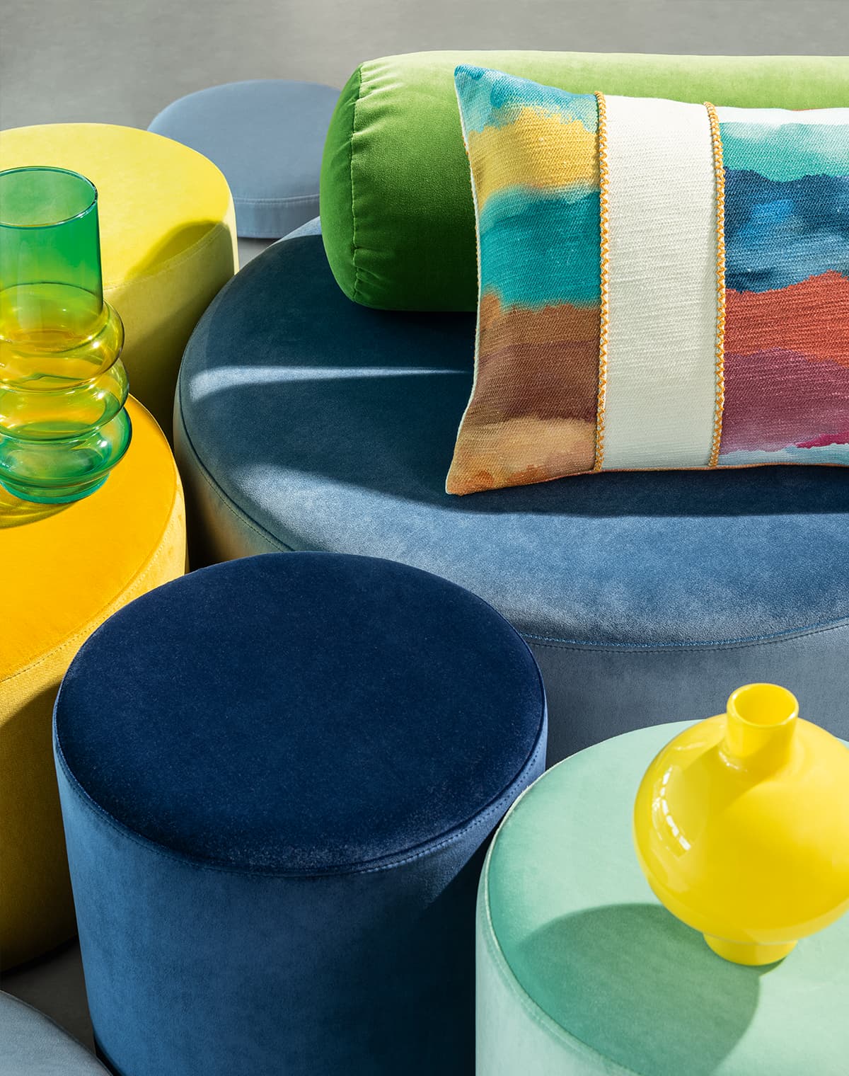 Blaue, grüne und gelbe Poufs und ein buntes Kissen.
