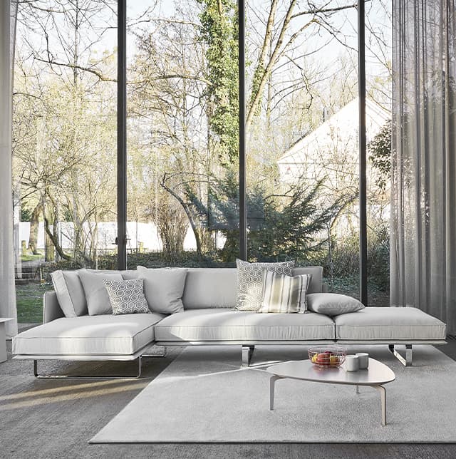 Graues Sofa mit Longchair in einemm hellen Zimmer mit einer großen Fensterfront