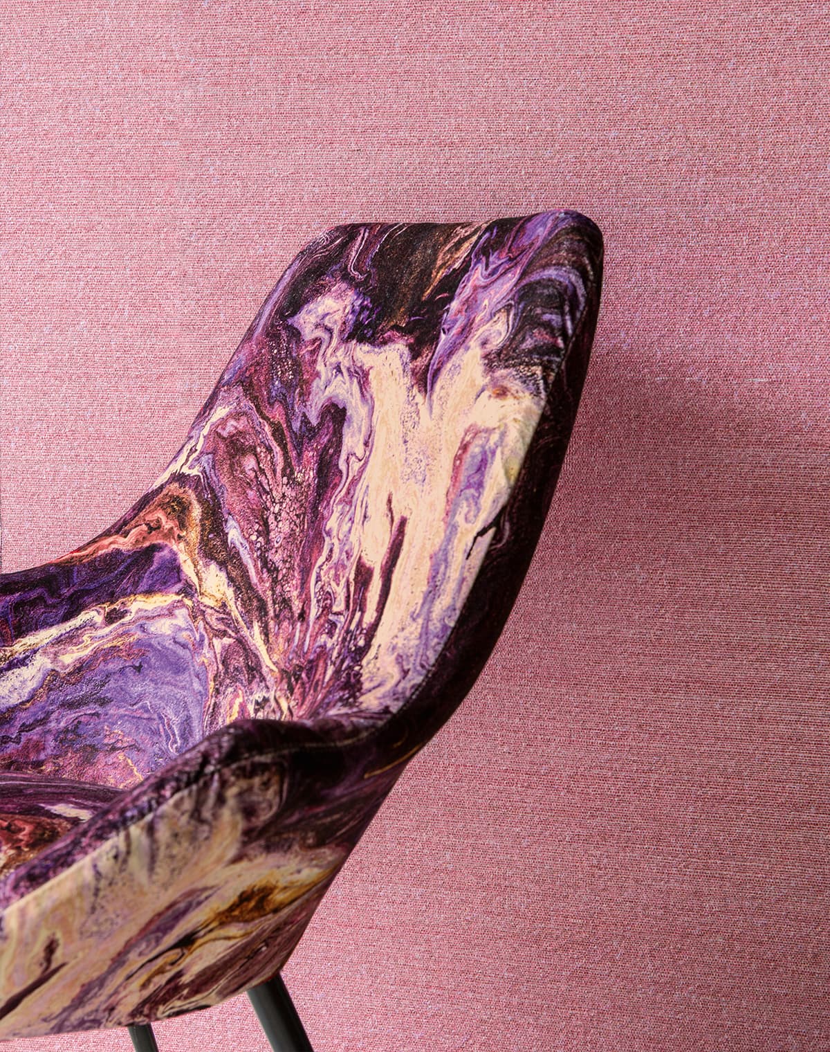Das Bild zeigt eine Nahaufnahme eines Sessels mit Lava-artigem Farbverlauf. Im Hintergrund ist eine Wand aus rosa Stoff zu sehen, die einen sanften Kontrast zum Sessel bildet.