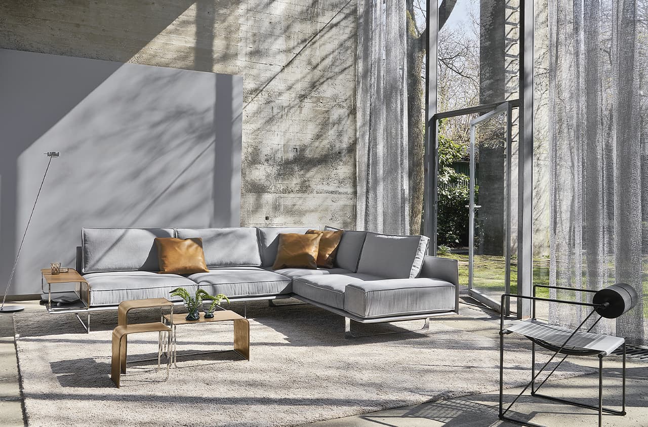 Graues Sofa mit braunen Deko-Kissen in einem hellen Raum mit großer Fensterfront